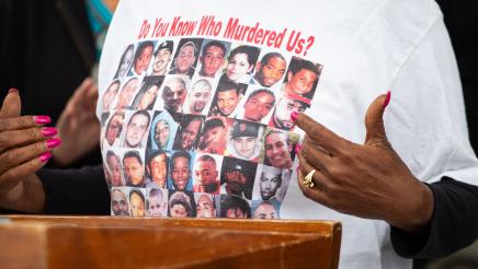 Guest speaker at podium, displaying printed shirt depicting victims