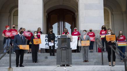 Asm. Gipson speaking, with members holding signs on steps