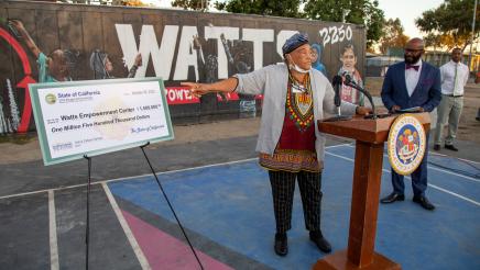 Guest speaker at podium, speaking, with large check on stand at left