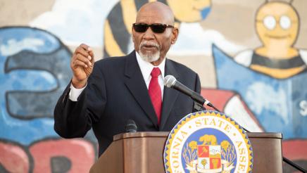 Guest speaker at podium, speaking, with mural in background