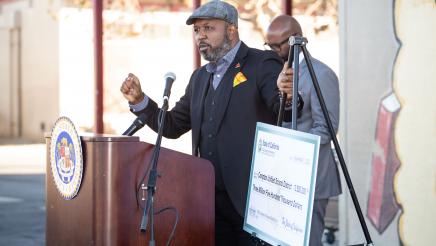 Guest speaker at podium, speaking, with hand on stand holding large check