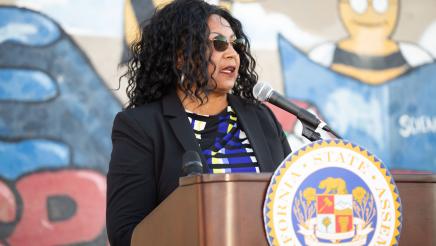 Guest speaker at podium, speaking, with mural in background