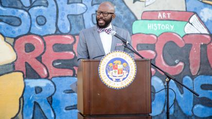 Asm. Gipson at podium, speaking, with mural in background