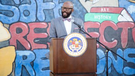Asm. Gipson at podium, speaking, with mural in background