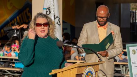 Guest speaker at podium, speaking, as Asm. Gipson listens on