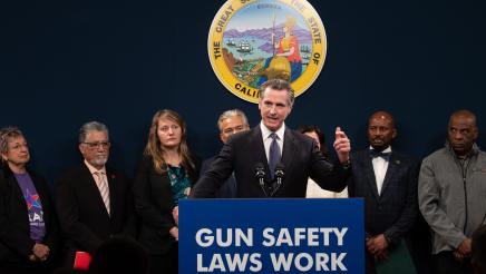 Gov. Newsom at podium, speaking, with Asm. Gipson and other legislators