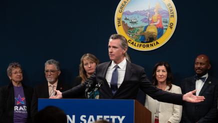 Gov. Newsom at podium, holding arms out to each side, with Asm. Gipson and other legislators