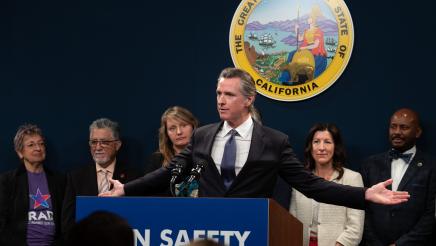 Gov. Newsom at podium, holding arms out to each side, with Asm. Gipson and other legislators