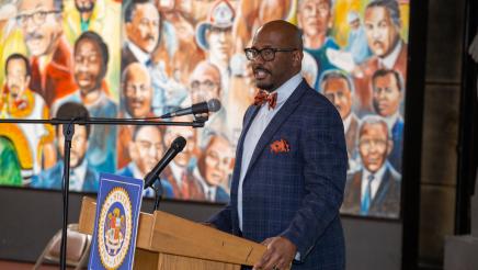 Asm. Gipson at podium, speaking, with mural in background