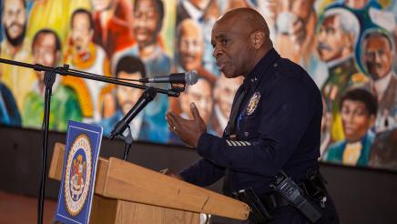Police officer at podium, speaking, with mural in background