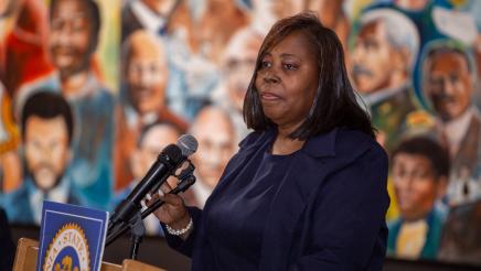 Guest speaker at podium, speaking, with mural in background