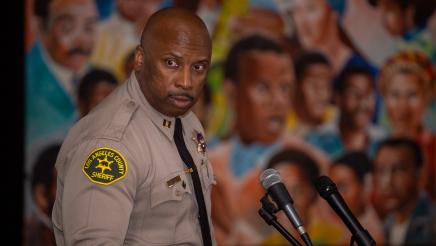 Sheriff at podium, speaking, with mural in background