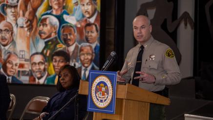Sheriff at podium, speaking, with mural in background