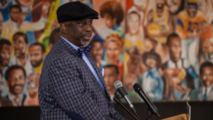 Guest speaker at podium, speaking, with mural in background