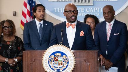 Asm. Gipson at podium, speaking, as Rep. Justin Jones listens on