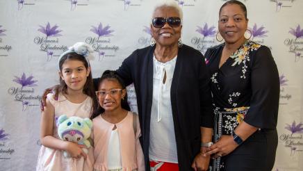 Mrs. Le Cresha Gipson with attendee and children with brand wall in background, featuring event logo