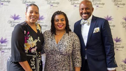 Asm. Gipson, Mrs. Le Cresha Gipson and guest with brand wall in background, featuring event logo