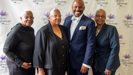 Asm. Gipson and attendees with brand wall in background, featuring event logo