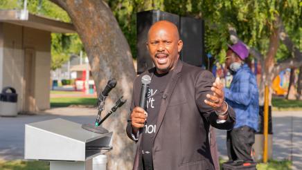 Asm. Gipson at podium, speaking and gesturing toward HR 36 poster
