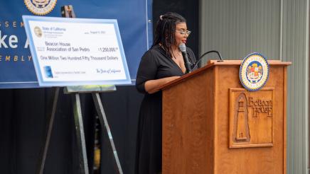 Guest speaker at podium, speaking, with large ceremonial check at left