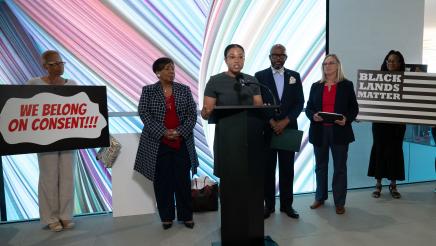 Jade Stevens at podium, speaking, as Asm. Gipson, Julie Alvis and others listen on