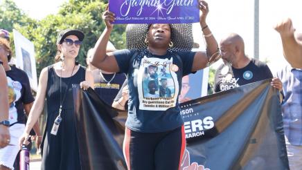 Marcher holding up colorful sign, with Asm. Gipson and others behind, holding banner