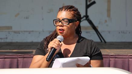 Speaker standing behind coffin, holding microphone and papers