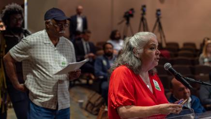 Audience member speaking at podium, with other audience members waiting to speak