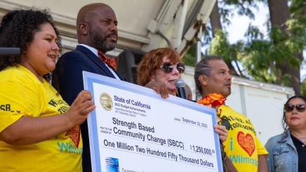 Asm. Gipson and SBCC staff on stage, holding up large ceremonial check