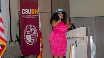 Woman in pink dress at podium, speaking