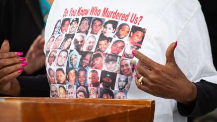 Guest speaker at podium, displaying printed shirt depicting victims