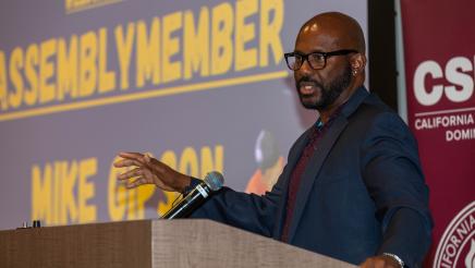 Asm. Gipson at podium, speaking, and gesturing with one hand