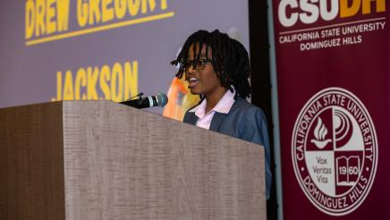 Youth at podium, speaking, with CSUDH banner in background