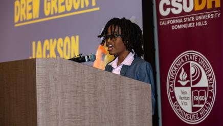 Youth at podium, speaking, with CSUDH banner in background