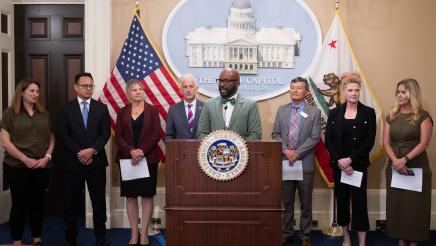 Asm. Gipson at podium, speaking, with ports representatives standing in support