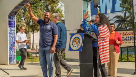 Asm. Gipson holding up fist as guest speaker speaks at podium
