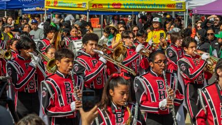 Band marching past resource tents, with many onlookers