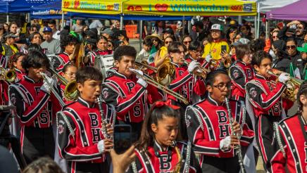 Band marching past resource tents, with many onlookers