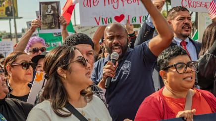 Asm. Gipson, holding up a fist and speaking into microphone, with fellow marchers