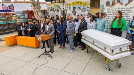 Wide view of Asm. Gipson, guest speakers, supporters and a white casket