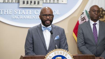 Asm. Gipson at podium, speaking, as Dr. BJ Snowden listens on