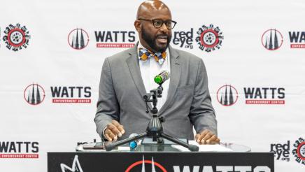 Asm. Gipson speaking at podium with logo backdrop in background