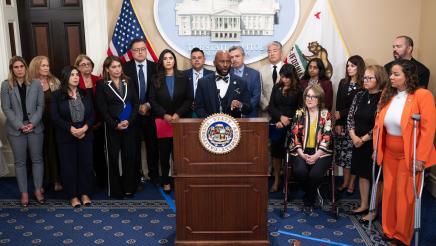 Asm. Gipson at podium, speaking, as legislators and guests listen on
