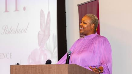 Woman in lavender blouse at podium, speaking